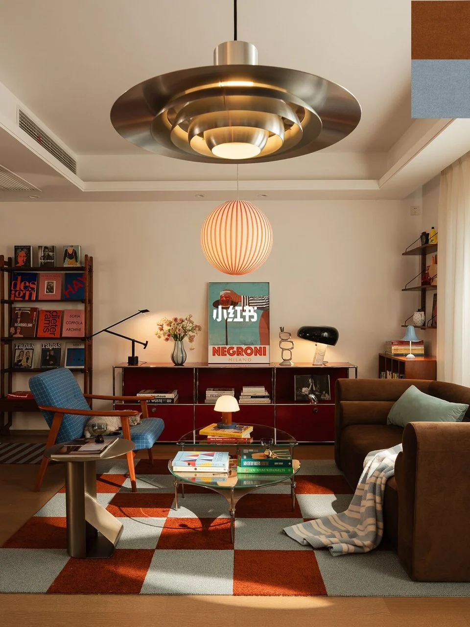 Brown sofa and blue armchair around a glass table on a rust and blue checker rug, with burgundy storage and paper lighting.