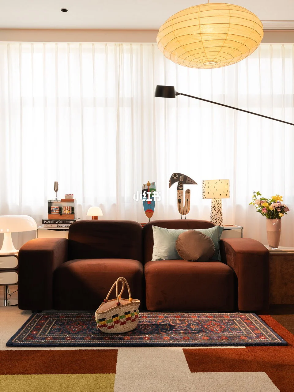 Brown sofa with green and round brown cushions, layered patterned rugs, a large paper pendant and a black floor lamp.
