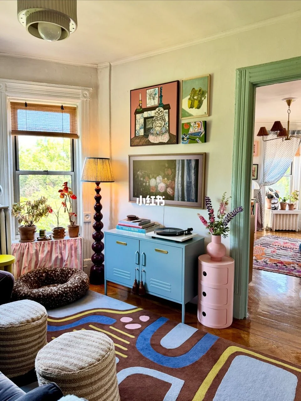 Pale blue and pink cabinets, colorful gallery wall, patterned rug and striped poufs beside a green doorway.