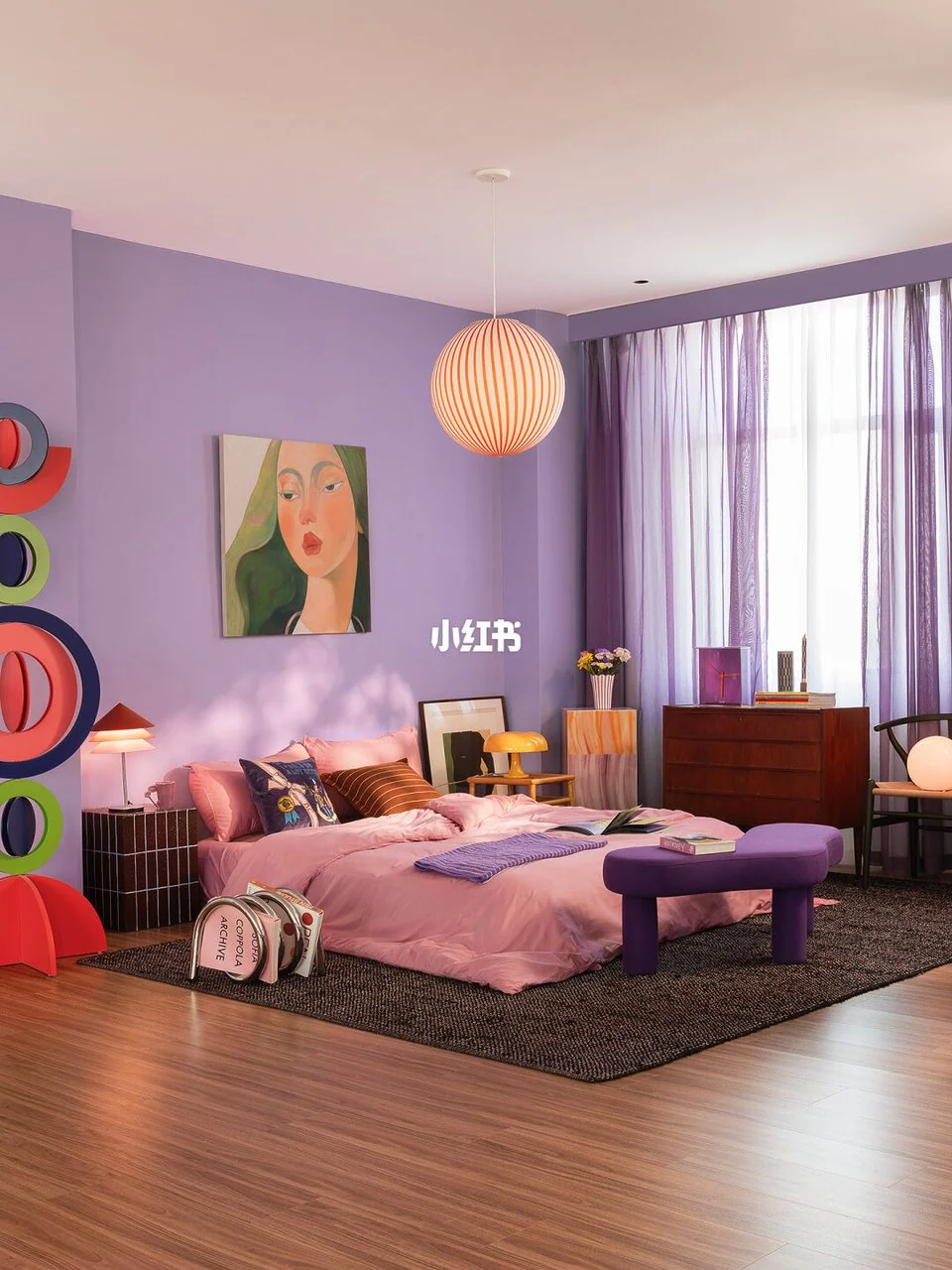 Lavender bedroom with pink bedding, a purple bench, orange striped pendant and several small colorful lamps.
