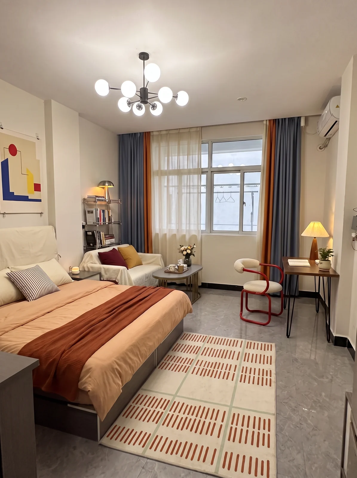 Proposed peach and red rental concept with warm bedding, cream sofa cover, red reading chair and graphic rug over gray tile.