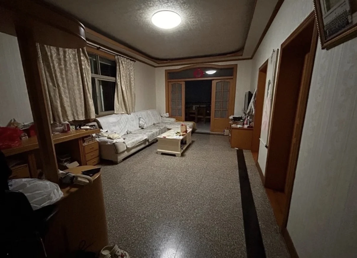Original older living room with gray terrazzo floor and dark border, pale sofa and wood door frames and ceiling trim.